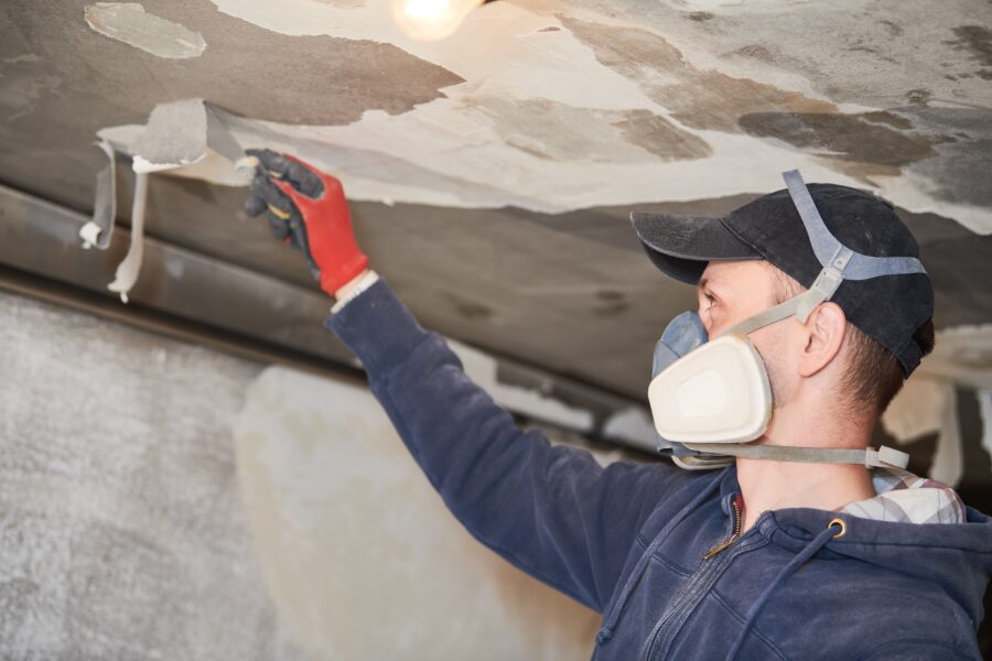 Worker with mask on scrapping at blackened ceiling with fire damage