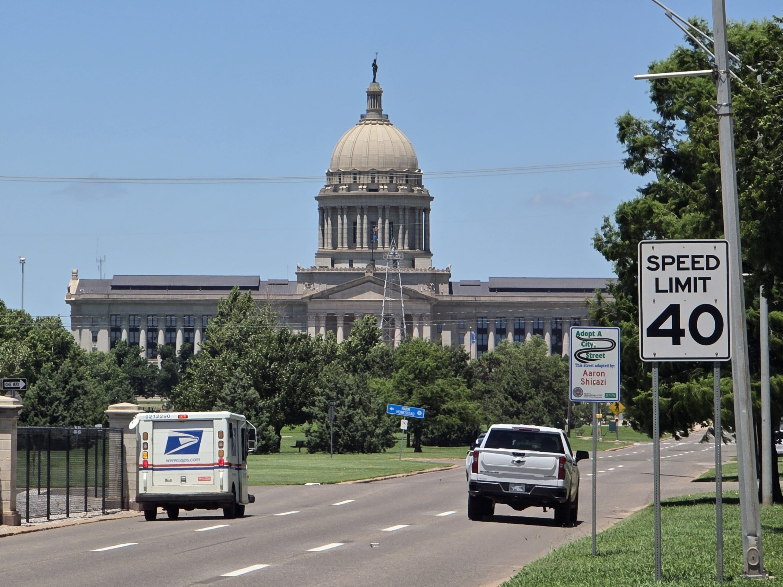 A view along Lincoln Boulevard of the Oklahoma State Capitol Building in OKC. A pickup truck and a USPS truck on the road. 